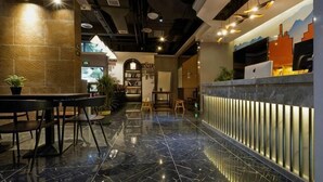 Um saguão de hotel moderno com piso de mármore, balcão de recepção, área de estar e uma estante de livros.