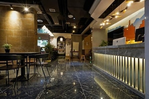 En modern hotellobby med ett marmorgolv, en receptionsdisk, en sittgrupp och en bokhylla.