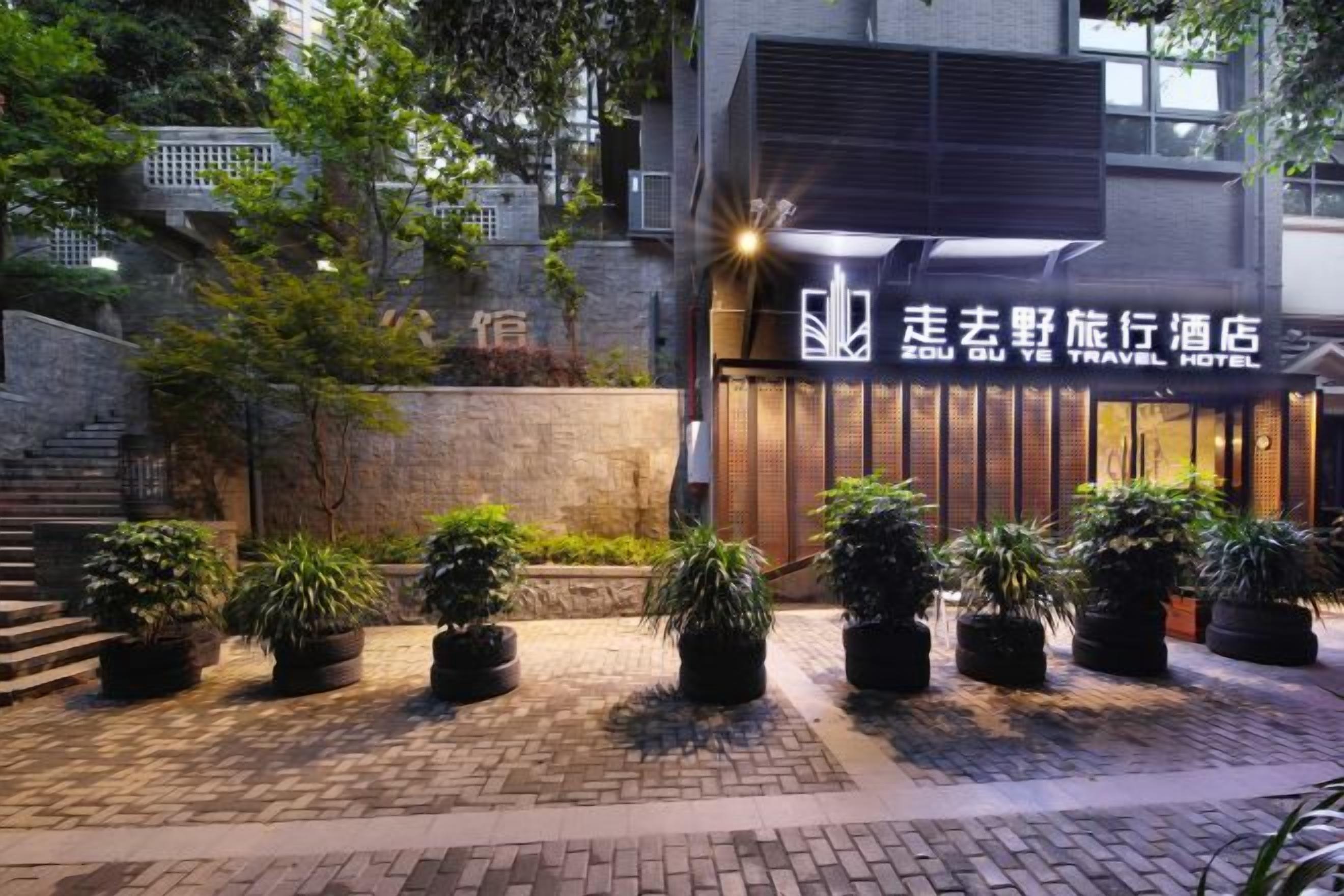 A hotel entrance with a sign, potted plants, and a brick pathway.