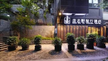 A hotel entrance with a sign, potted plants, and a brick pathway.