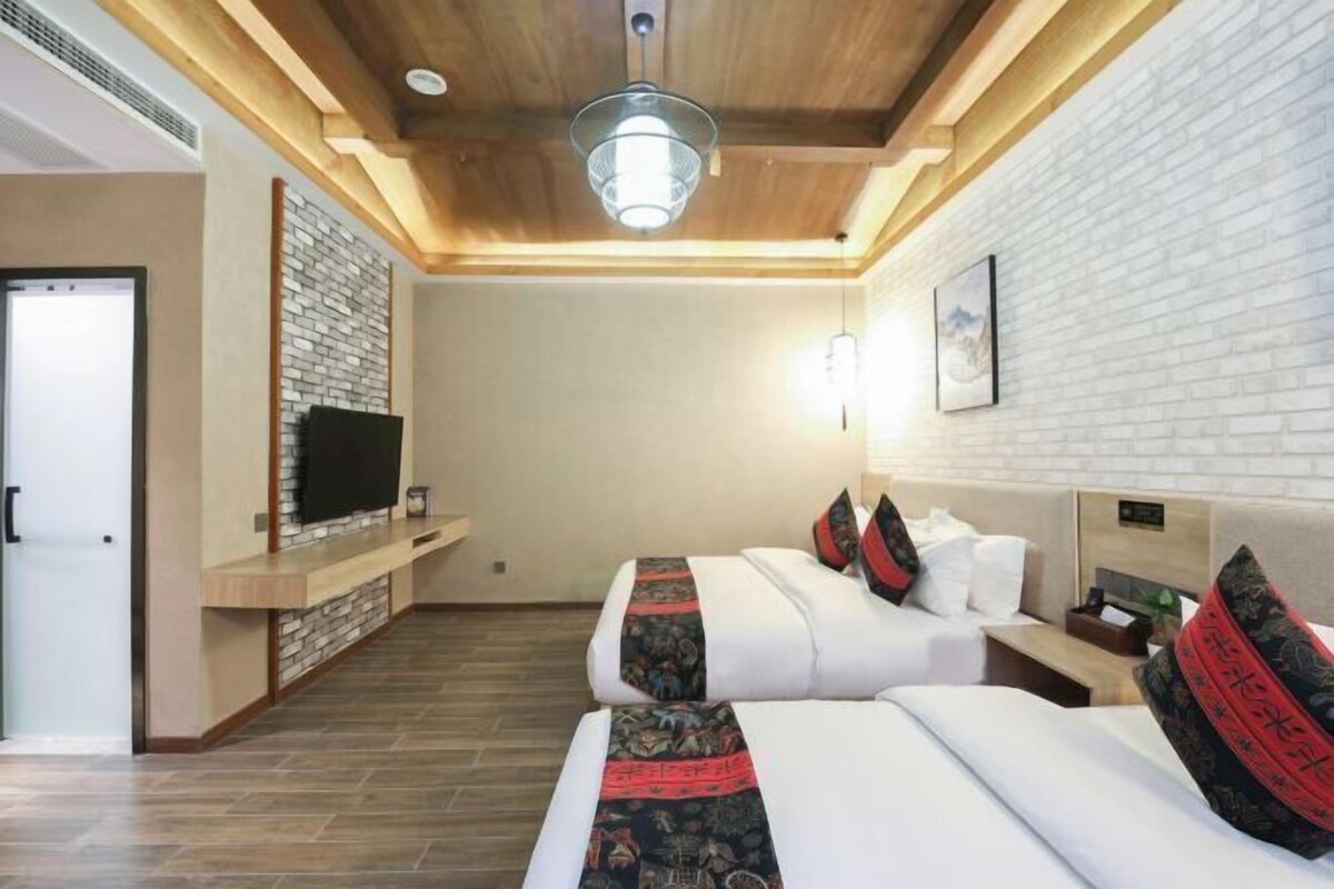 A hotel room with two beds, a TV, a brick wall, and a wooden ceiling.