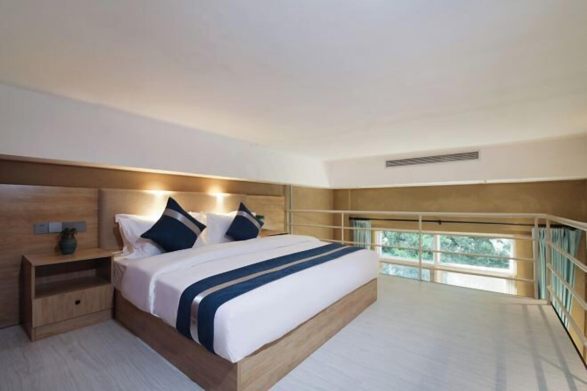 A modern bedroom with a large bed, bedside tables, and a view of greenery through a balcony.