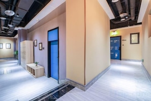 A hotel corridor with a blue door, a small table with a plant, and framed pictures on the walls.