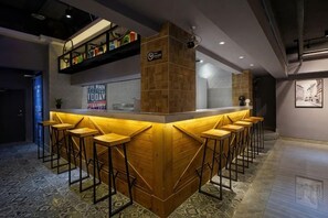 Uma área de bar com balcão de madeira, vários banquinhos e uma prateleira com garrafas.