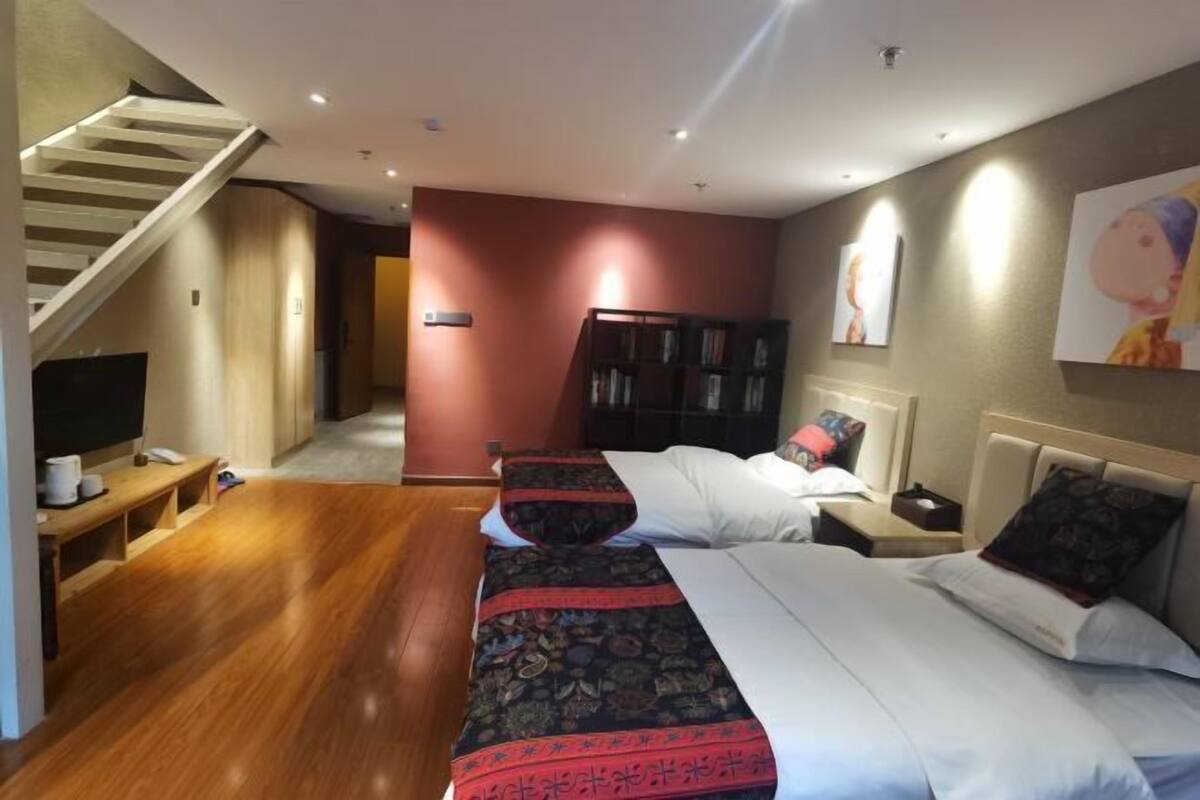 Ein Hotelzimmer mit Holzboden, einer Treppe, einem Bücherregal, einem Bett mit gemustertem Überwurf und einem Bild an der Wand.