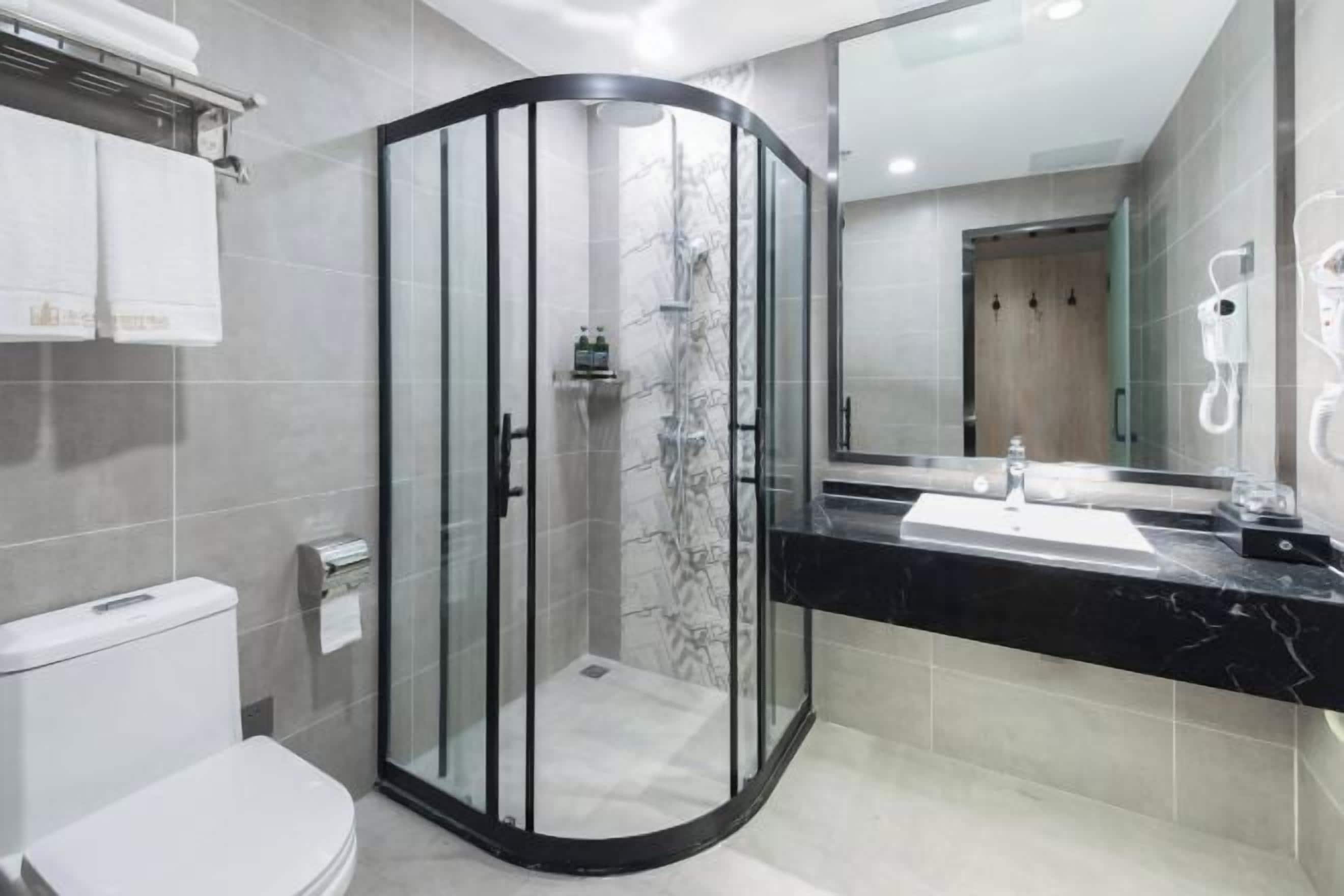 Un baño moderno con ducha envuelta en vidrio, inodoro, lavamanos con encimera negra y espejo.