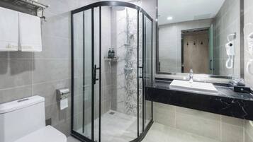 Un baño moderno con ducha envuelta en vidrio, inodoro, lavamanos con encimera negra y espejo.
