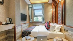 Quarto de hotel com uma cama, duas mesas de cabeceira com livros, um laptop, uma televisão e uma janela com cortinas.