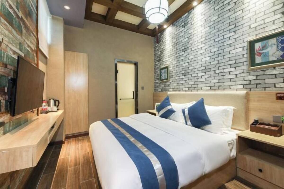 Ein Hotelzimmer mit Bett, Nachttisch, Schrank, Spiegel, einem an der Wand montierten Fernseher und einer Wand mit Backsteinmuster.