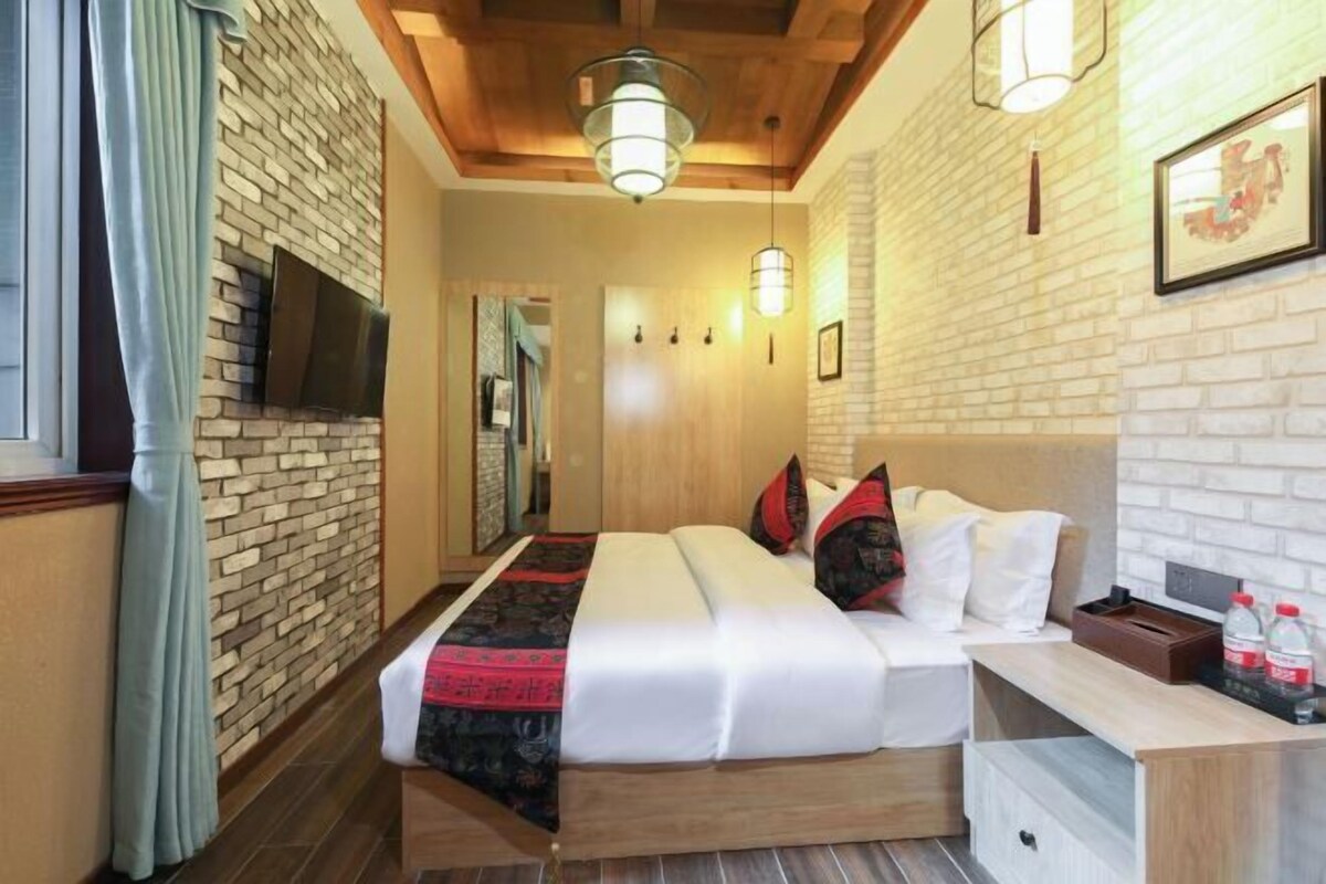 A hotel room with a brick wall, a wooden ceiling, a bed with white bedding, a bedside table, and a mounted TV.