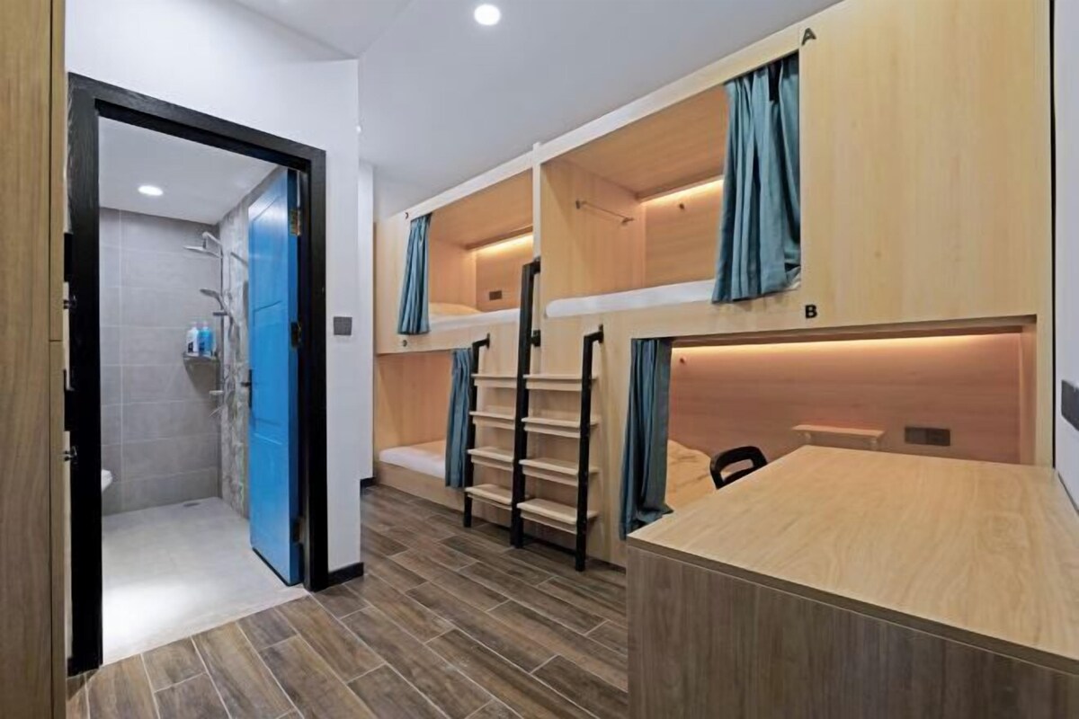A room with bunk beds, a desk, and a shower area.
