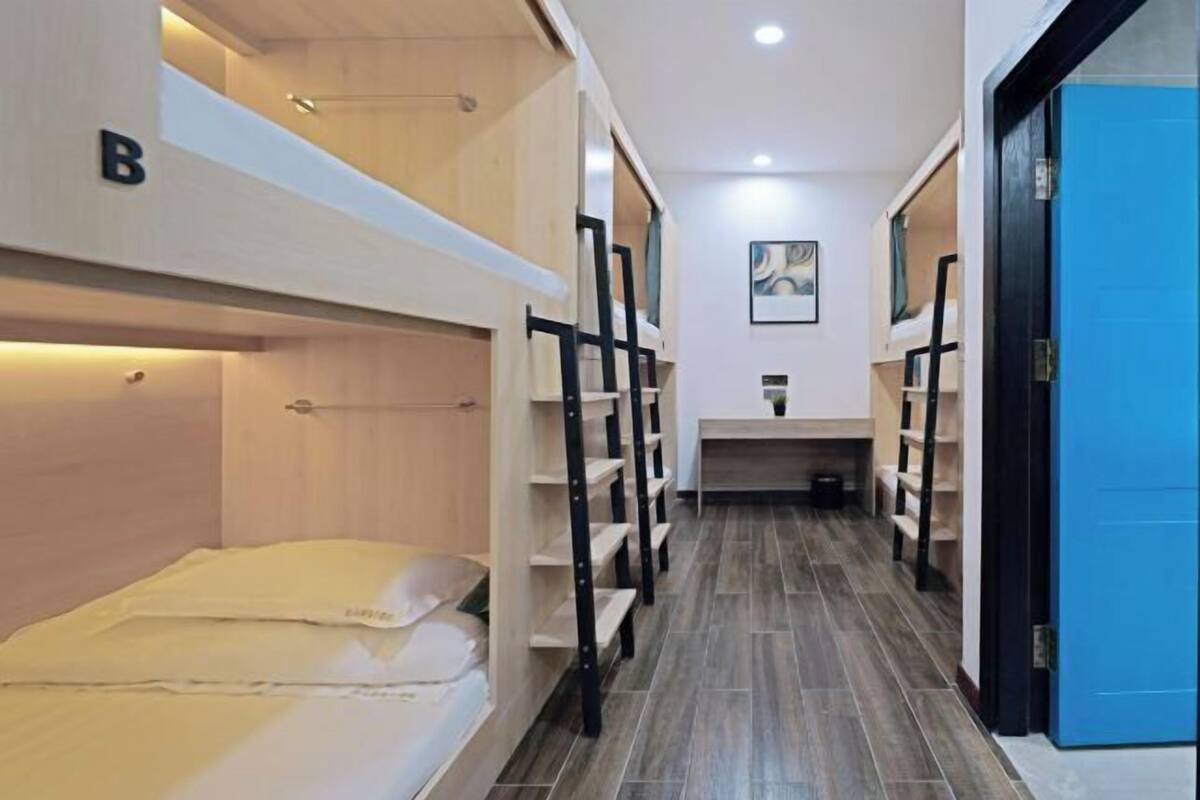 Ein Hotelzimmer mit Stockbetten, einem kleinen Schreibtisch und einem Badezimmer mit Waschbecken und Spiegel.
