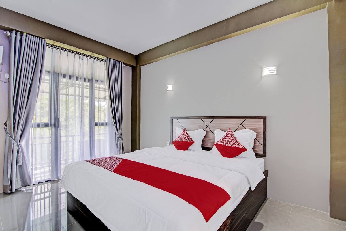 Ein modernes Hotelzimmer mit einem großen Bett, einer Kopfteil mit geometrischen Mustern und Blick ins Freie durch das Fenster.