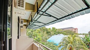 A balcony with a metal roof, a view of a building with a blue roof, and surrounding greenery. - Hotel O Penginapan Thoybah Syariah Near Pondok Pesantren UMAR BIN KHATAB km 9 garuda sakti (Pekanbaru)