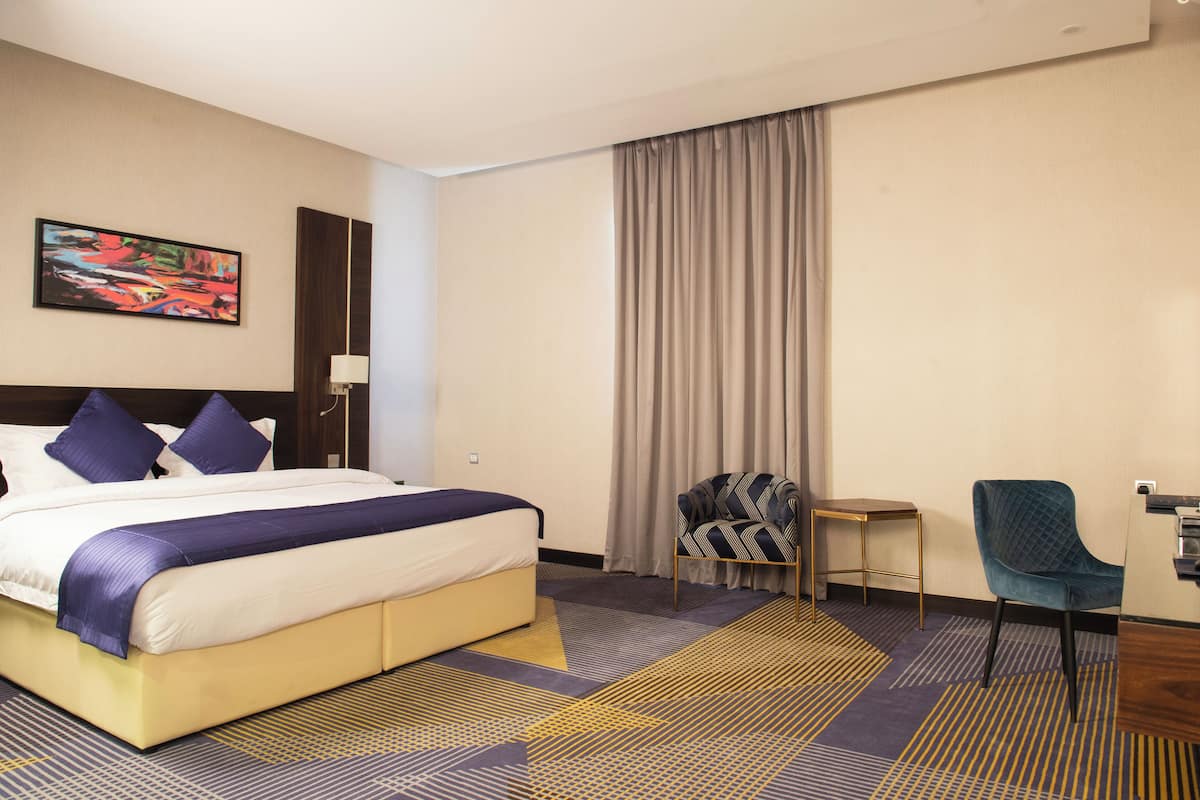 A hotel room with a large bed, a chair, a small table, and a painting on the wall.