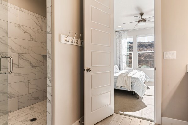 Une salle de bain carrel ée de marbre, avec une douche et une porte donnant sur une chambre à coucher équipée d’un lit et d’une fenêtre.