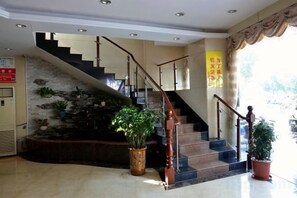 A hotel lobby with a staircase, potted plants, and a stone wall. - Jade Business Hotel (Jade Street, Pingzhou, Foshan) (Foshan)