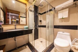 Un baño moderno con ducha envuelta en vidrio, inodoro blanco y lavamanos sobre encimera negra.