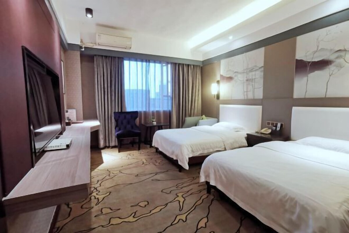 Habitación de hotel con dos camas, un escritorio, una silla y un amplio ventanal con cortinas.