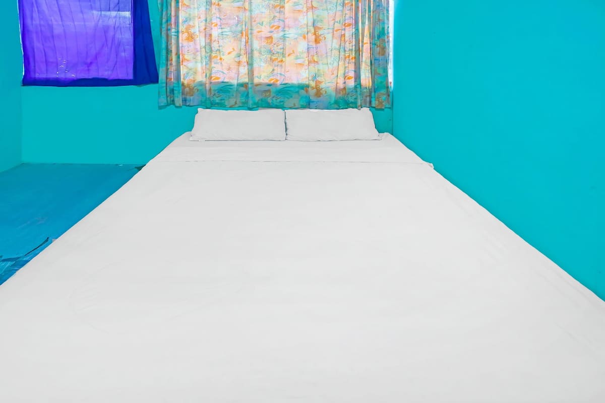 Een bed met witte lakens in een kamer met turquoise wanden en een bloemen gordijn.