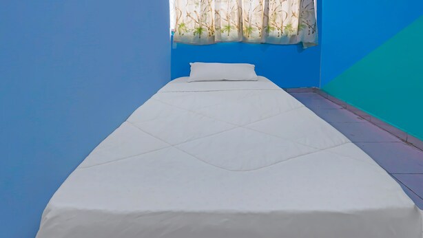 A single bed with a white mattress and pillow in a room with blue walls and a window with a bamboo curtain. - Hotel O Kurnia ShangrilaNearNagoya Hill Shopping Mall (Batam)