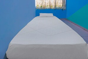 A single bed with a white mattress and pillow in a room with blue walls and a window with a bamboo curtain. - Hotel O Kurnia ShangrilaNearNagoya Hill Shopping Mall (Batam)