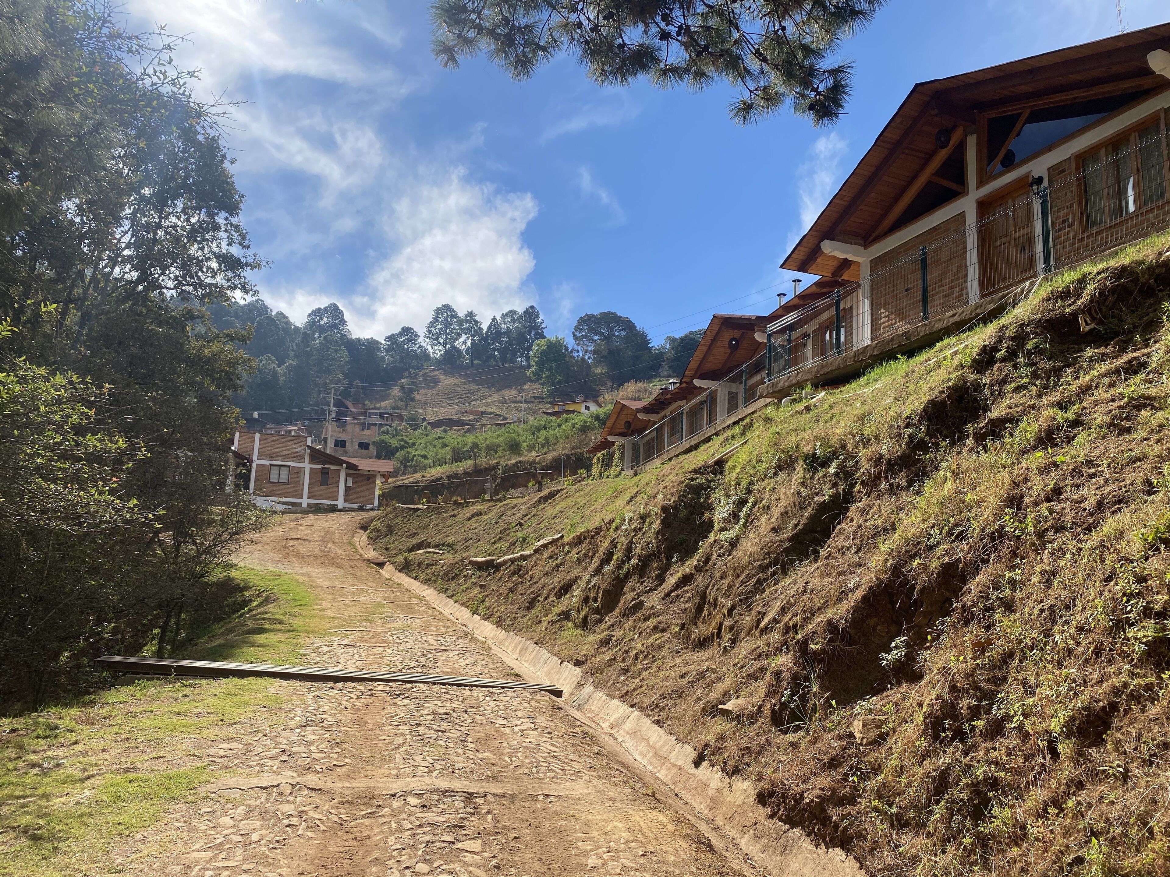 Un camino en la ladera de una colina con un sendero de tierra que lleva a una hilera de casas con techos de madera y paredes de ladrillo.