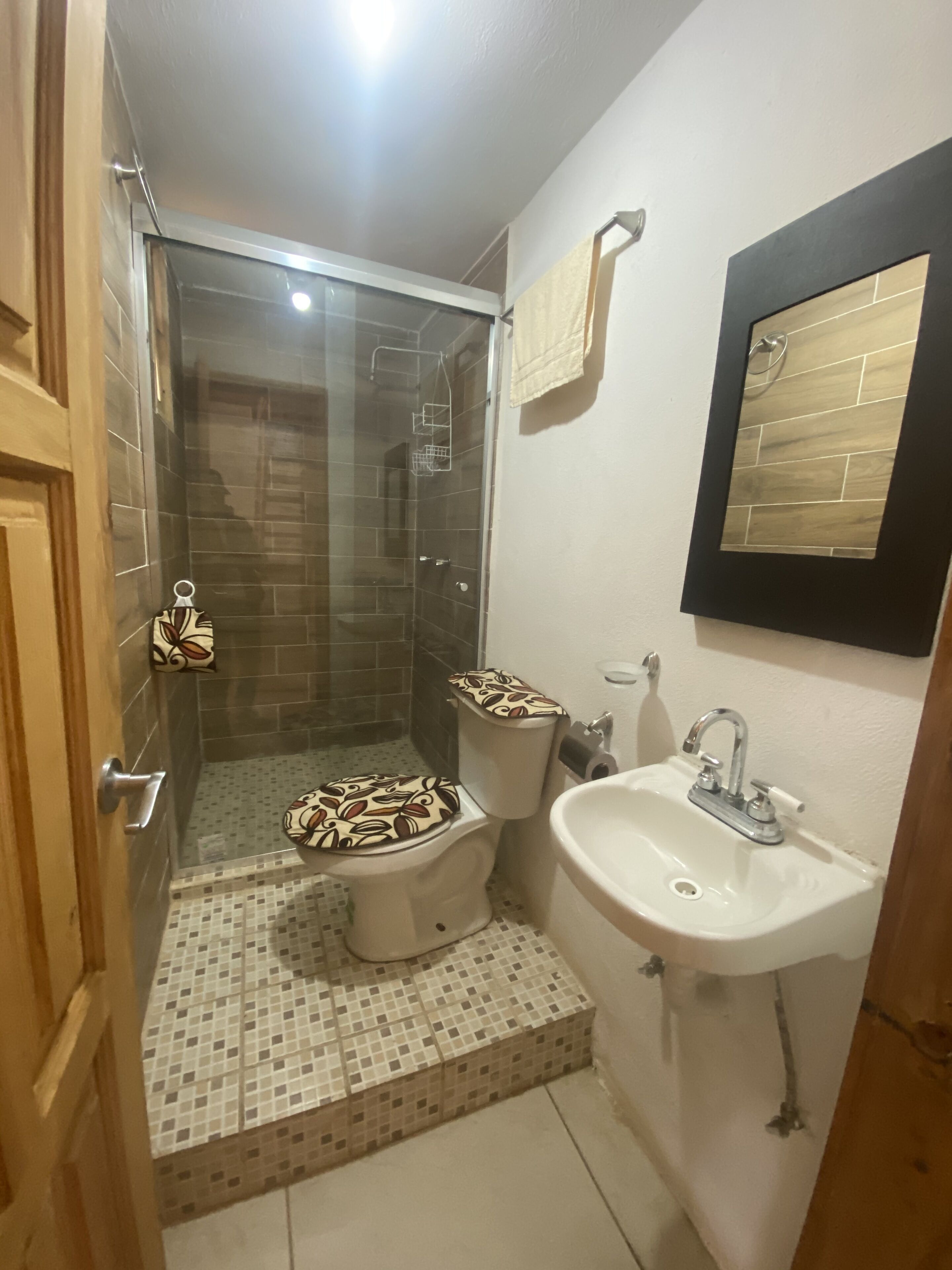 Un baño con ducha, dos inodoros, un lavamanos y un espejo.