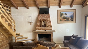 A living room with a brick fireplace, wooden staircase, and a glass coffee table. - Cabañas los Pirineos (Mazamitla)