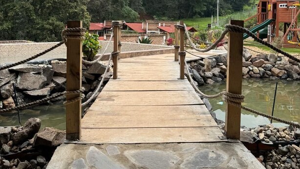 A wooden bridge with rope railings leading to a building with a red roof. - Cabañas los Pirineos (Mazamitla)