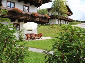 Ein traditionelles Chalet mit Holzbalkonen, einem Essbereich mit Tisch und Stühlen sowie einem weißen Sonnenschirm.