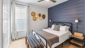 Ein Schlafzimmer mit einem Bett, Nachttischen, einem Deckenventilator und einem Fenster mit Vorhängen.