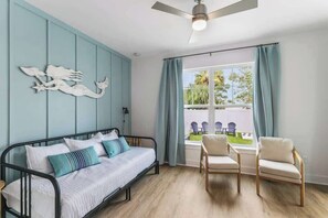 A bedroom with a bed, a ceiling fan, a window with curtains, and a view of the outside.