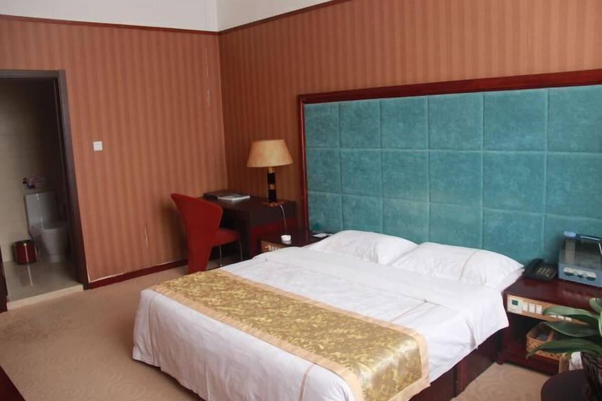 A hotel room with a bed, a desk, a chair, a lamp, and a telephone.