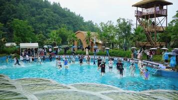 A swimming pool with people, surrounded by greenery and a wooden structure.