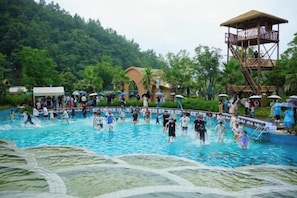 A swimming pool with people, surrounded by greenery and a wooden structure. - Xiuhe Hot Spring Holiday Hotel (Xiushui)