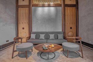 A modern living room with a grey sofa, two grey armchairs, and a wooden coffee table with fruits and a teapot. - Xiuhe Hot Spring Holiday Hotel (Xiushui)