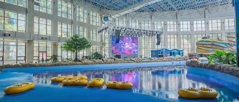 Una piscina interior con techos altos y ventanas amplias, rodeada de diversas atracciones acuáticas.