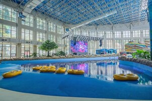 Una piscina interior con techos altos y ventanas amplias, rodeada de diversas atracciones acuáticas.