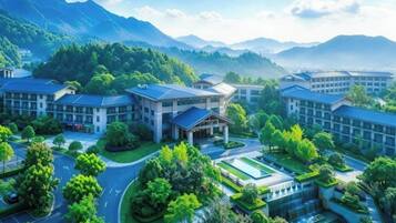 A modern hotel complex with multiple buildings, surrounded by lush greenery and mountains in the background.