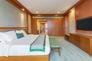 Habitación de hotel con una cama grande, televisión, armario de madera y una pequeña zona de estar.