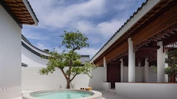 A traditional courtyard with a stone pool, wooden pergola, and a tree.