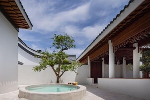 Un patio tradicional con una piscina de piedra, una pérgola de madera y un árbol.