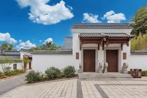 A traditional building with a tiled roof and wooden doors, surrounded by a paved area and greenery.