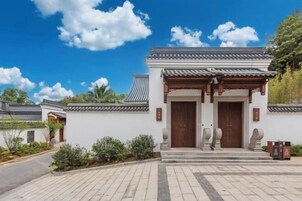 Un edificio tradicional con tejado de tejas y puertas de madera, rodeado de un área pavimentada y vegetación.