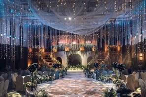 A banquet hall with a long table, draped ceiling, and decorative lighting.