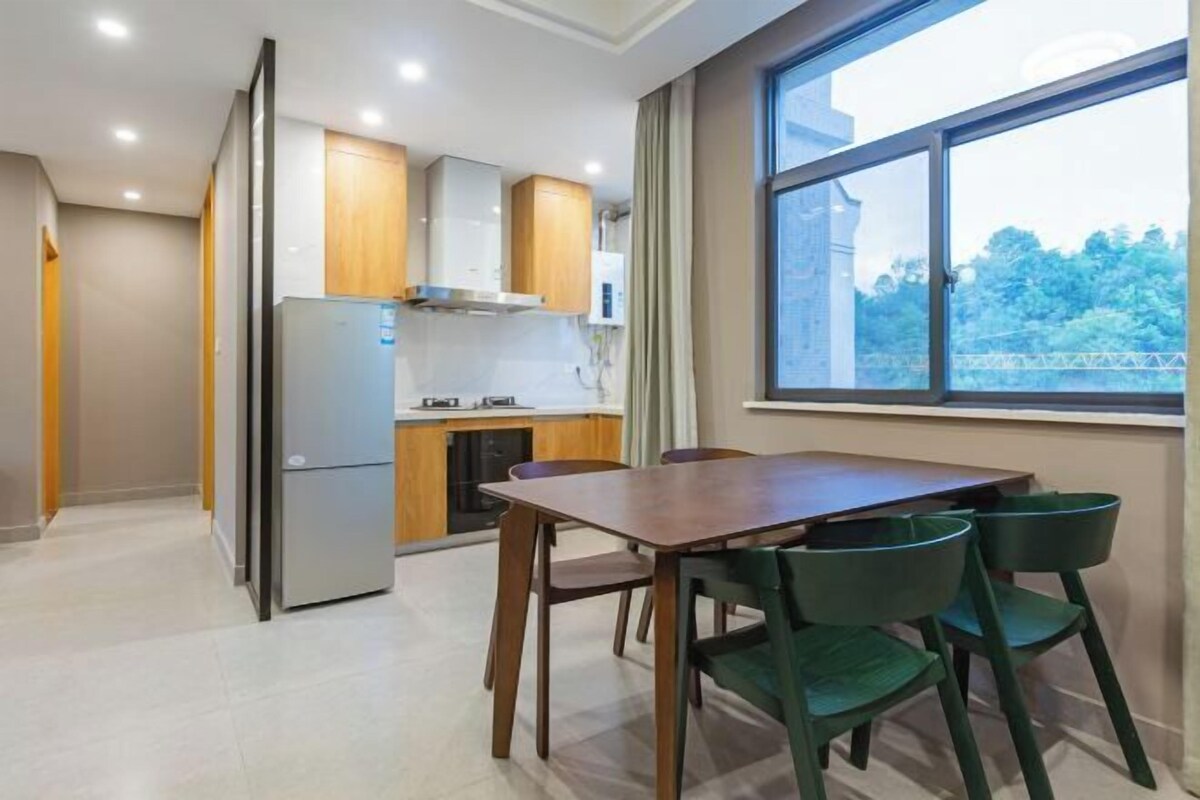 A modern kitchen with wooden cabinets, a stainless steel refrigerator, and a dining area with a wooden table and green chairs.