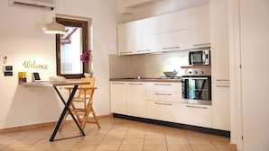 A modern kitchen with white cabinets, a built-in microwave, and an oven. There's a wooden table with a chair, a small potted plant, and a 'Welcome' sign on the wall. - Villa with garden - Porto Ada Pizzo - (Pizzo Calabro)