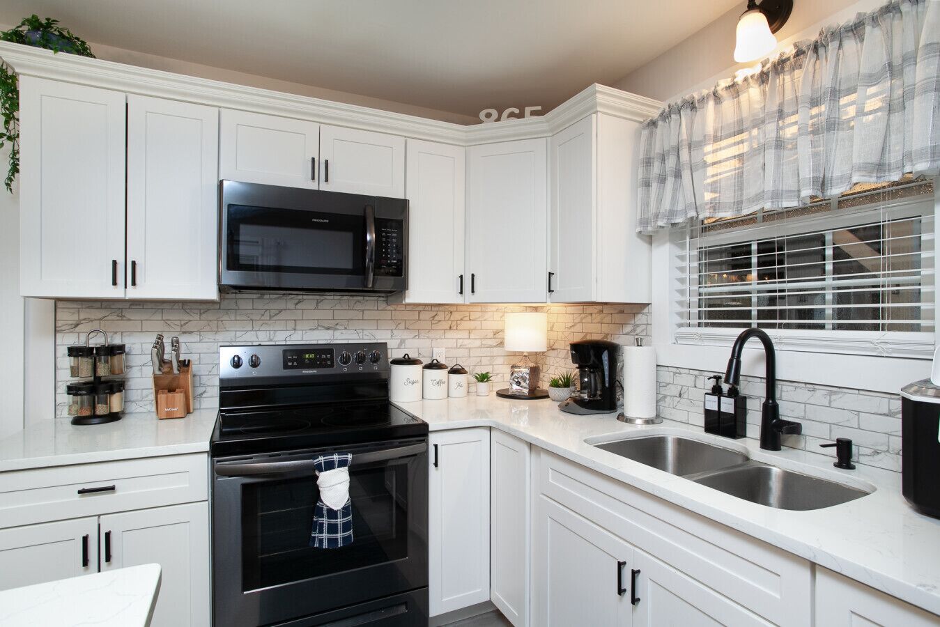 A kitchen with white cabinets, a black microwave, a stove, and a sink.