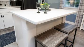 Una cocina con mostrador blanco, dos taburetes de madera y un recipiente de vidrio con limones y limas.